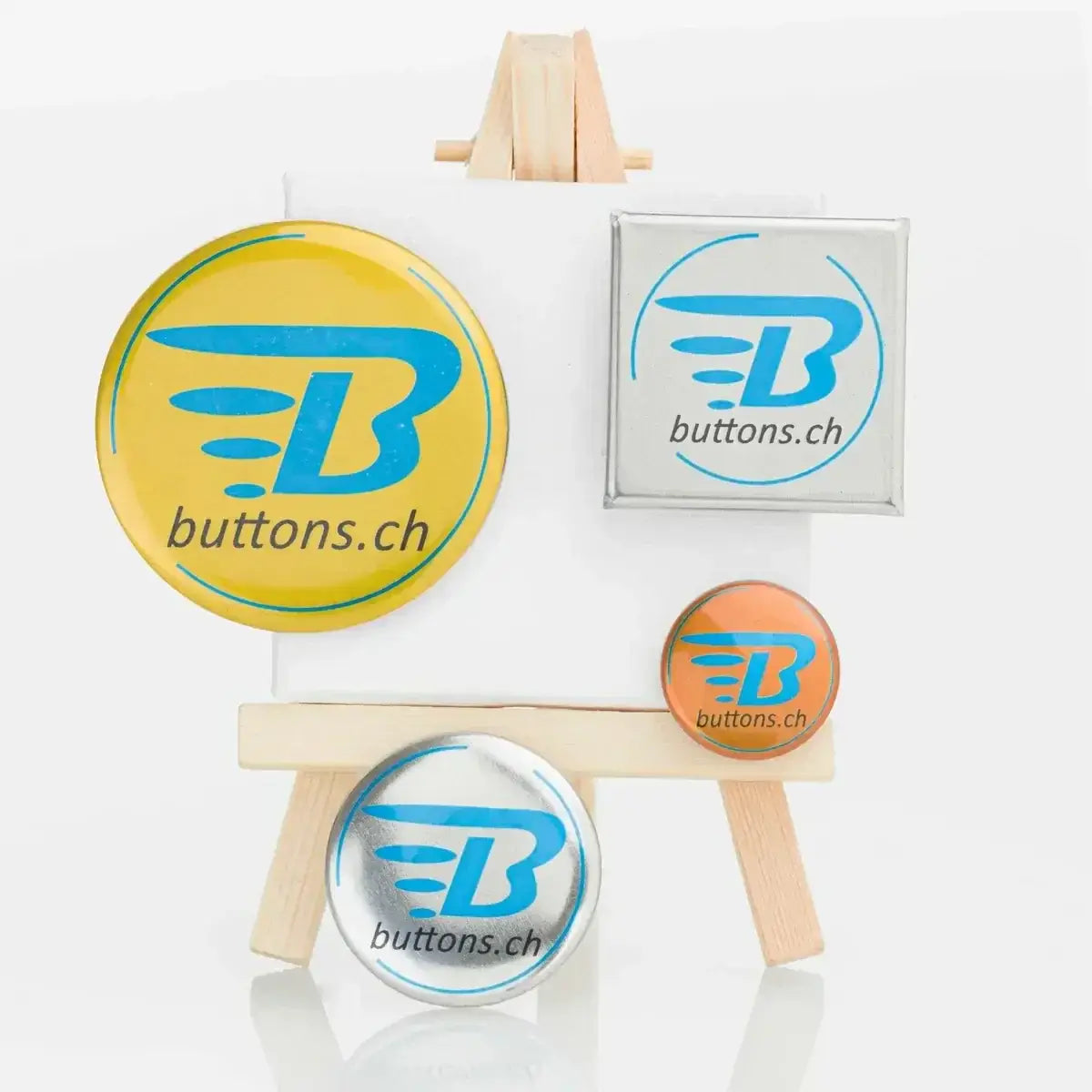 Gold-, silber- und bronzefarbene Metallic-Buttons mit blauem buttons.ch-Logo auf einer Staffelei.