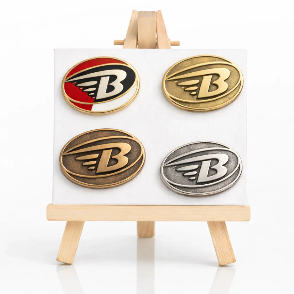 Verschiedene geformte Metallpins mit farbigen Motiven auf einer kleinen Staffelei.
