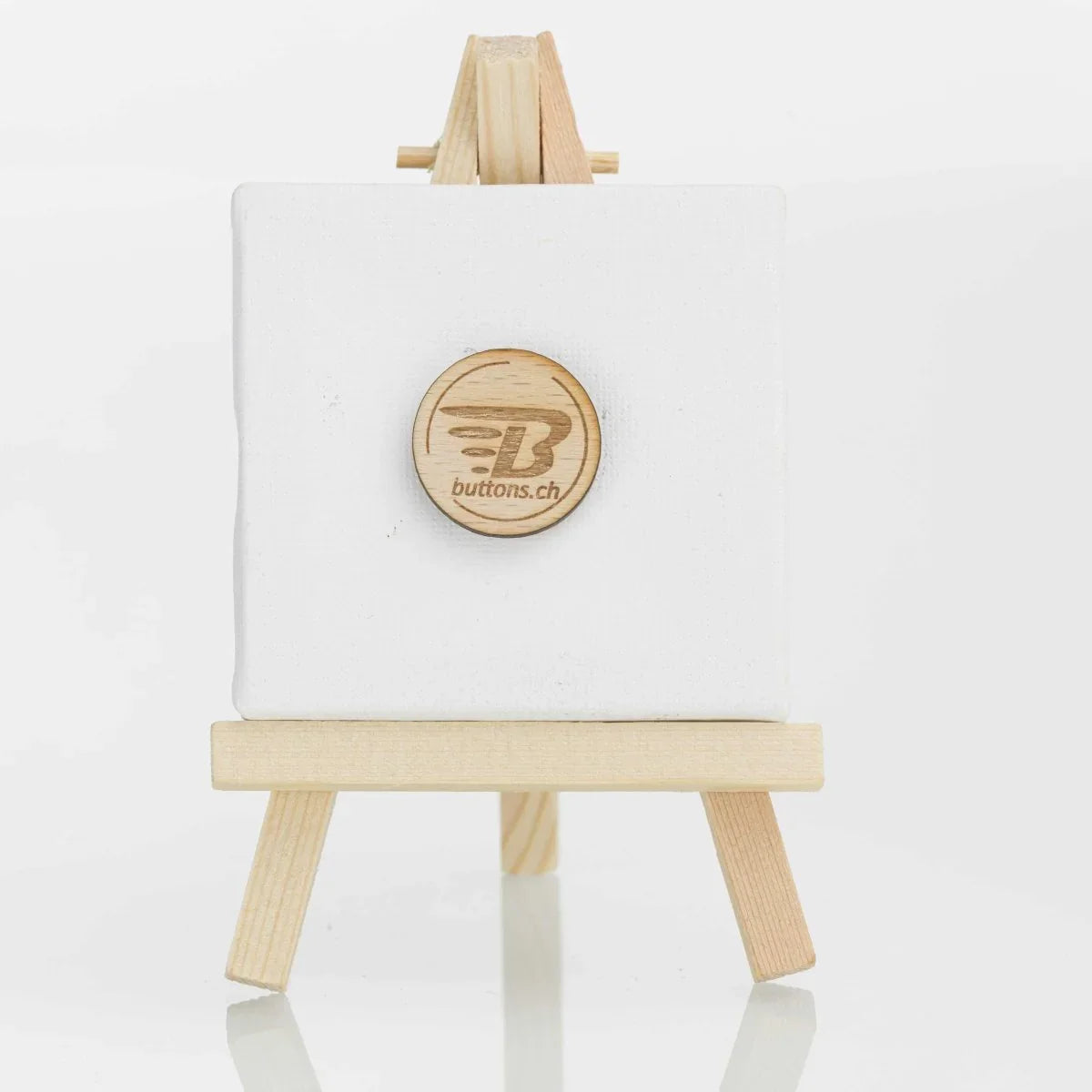 Runder Holz-Anstecker, 25 mm, mit eingraviertem buttons.ch-Logo auf einer kleinen Staffelei.