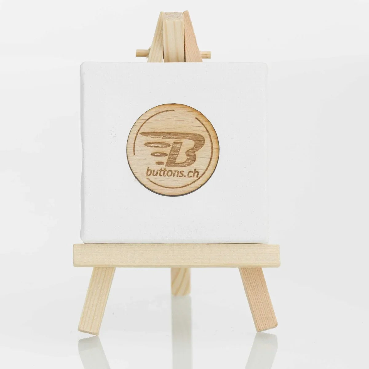 Runder Holz-Anstecker, 37 mm, mit eingraviertem buttons.ch-Logo auf einer kleinen Staffelei.