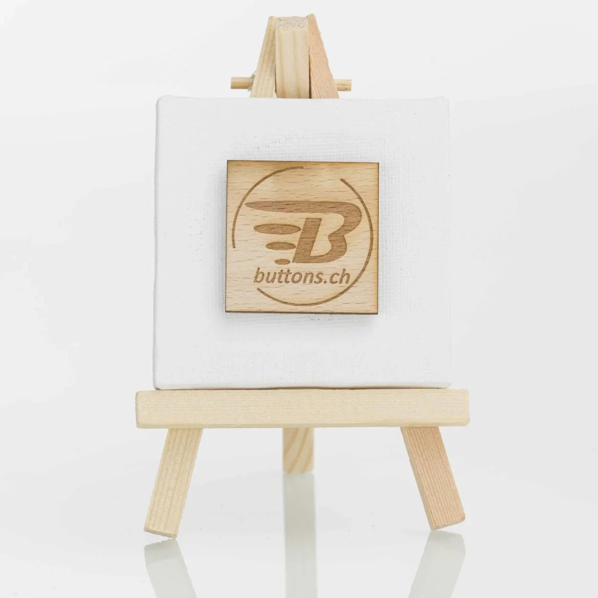 Quadratischer Holz-Anstecker, 37 × 37 mm, mit eingraviertem buttons.ch-Logo.