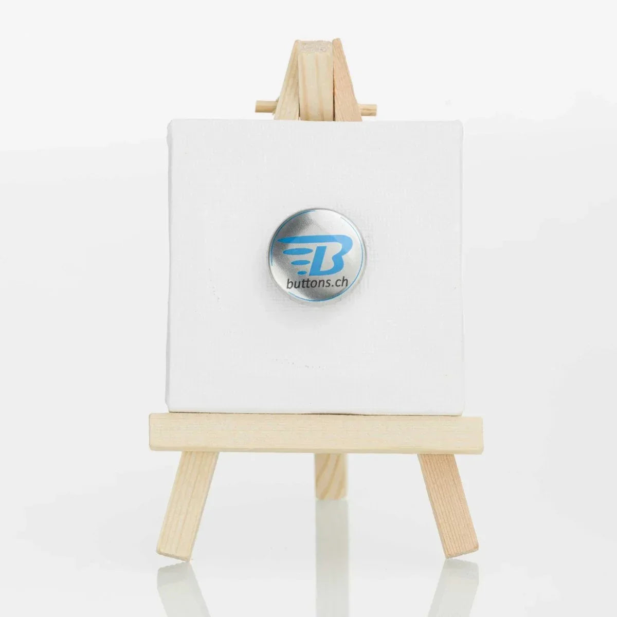 Runder Metallic-Button in Silber, 25 mm, mit blauem buttons.ch-Logo.