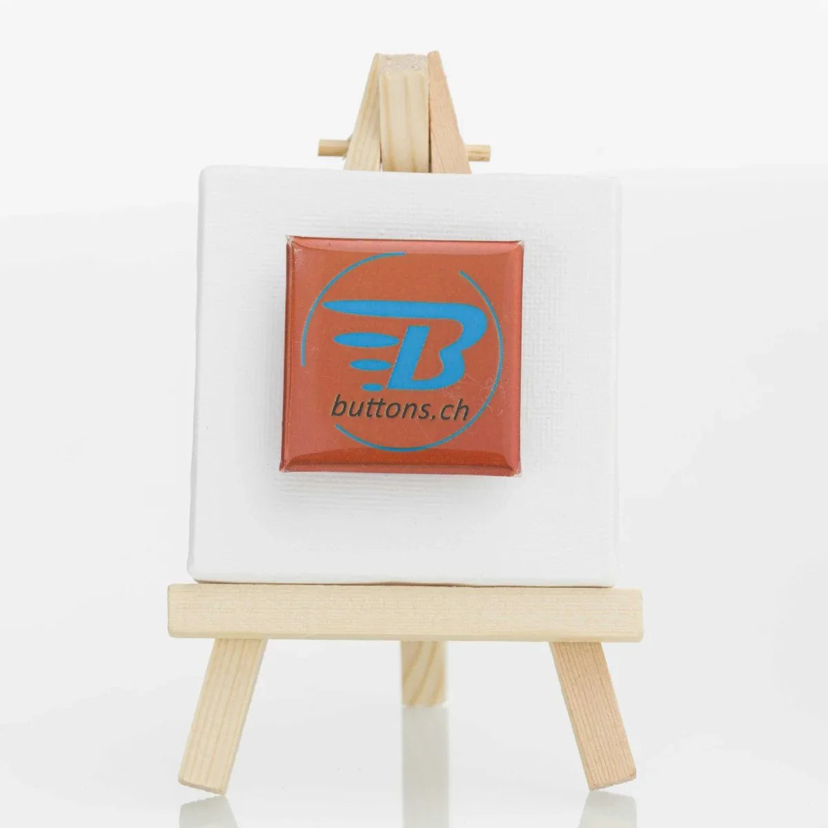 Quadratischer Metallic-Button in Bronze, 37 × 37 mm, mit blauem buttons.ch-Logo.