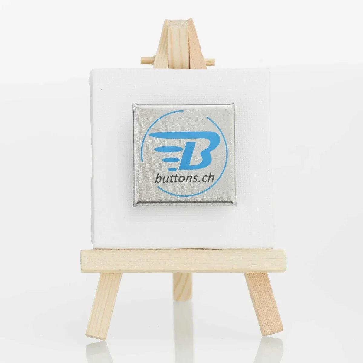 Quadratischer Metallic-Button in Silber, 37 × 37 mm, mit blauem buttons.ch-Logo.