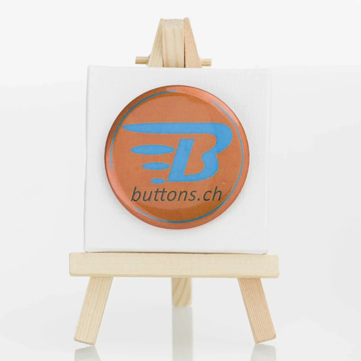 Runder Metallic-Button in Bronze, 56 mm, mit blauem buttons.ch-Logo.