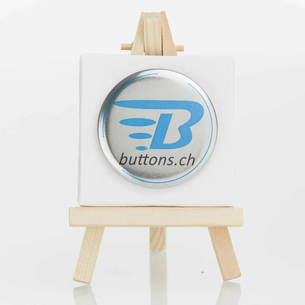 Runder Metallic-Button in Silber, 56 mm, mit blauem buttons.ch-Logo.