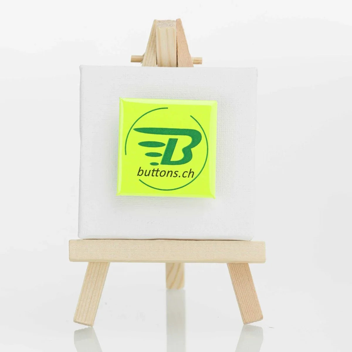 Quadratischer Neonbutton in Neongelb, 37 × 37 mm, mit buttons.ch-Logo.